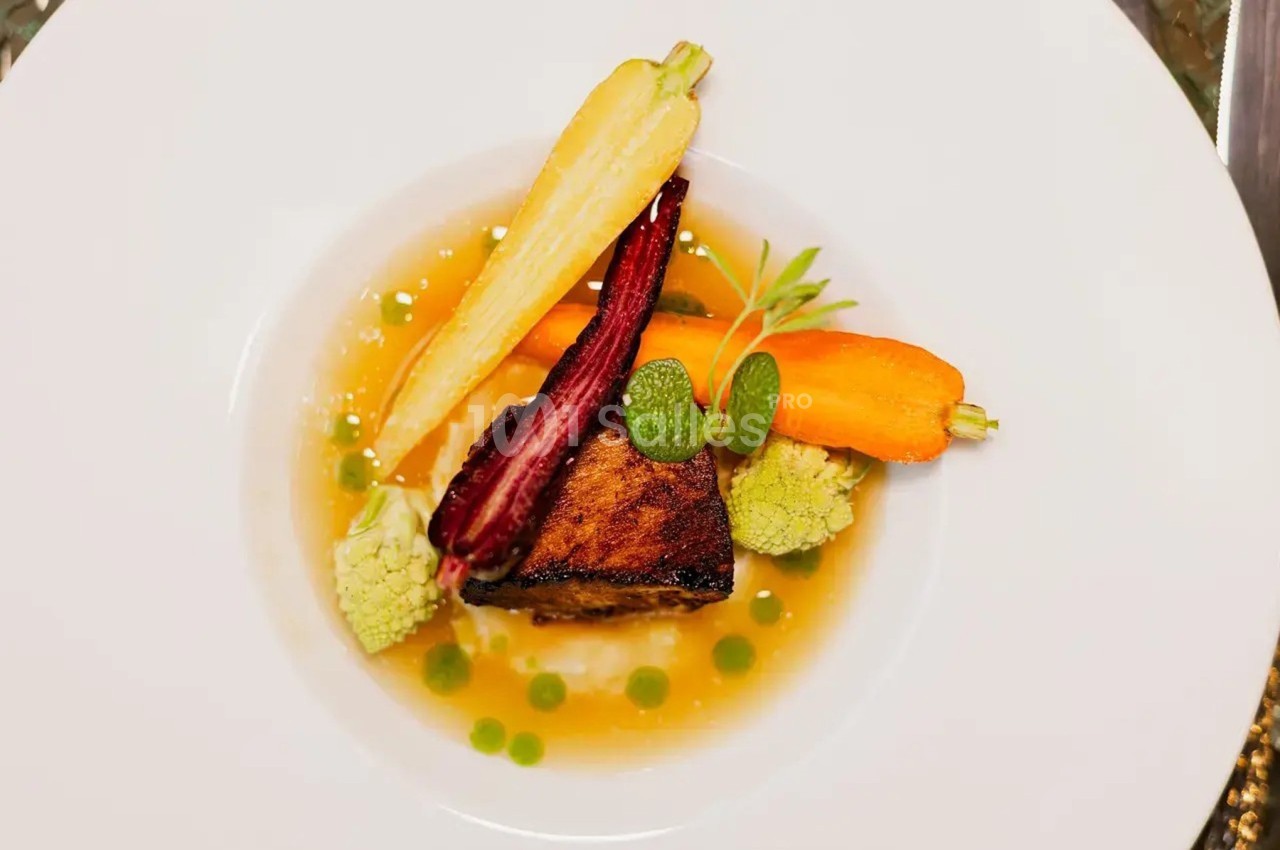 Assiette gastronomique avec un morceau de viande grillée, légumes colorés et sauce disposés de manière artistique.
