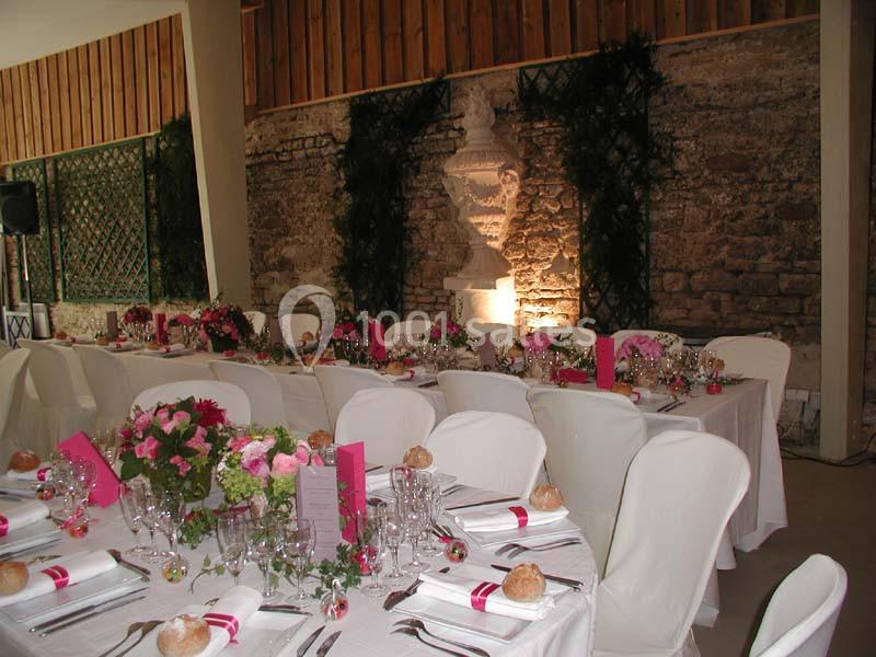 Salle de réception décorée avec des tables dressées, nappes blanches, fleurs roses et lumière tamisée.