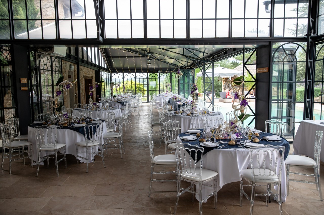 Salle de réception lumineuse avec tables décorées pour un événement, donnant sur une terrasse et une piscine extérieure.