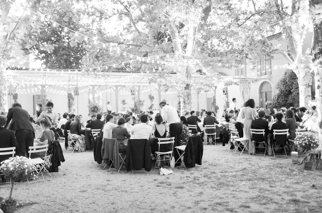 Groupe de personnes assises à des tables en extérieur, sous des guirlandes lumineuses, lors d'un événement festif.