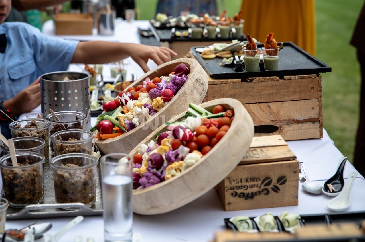 Buffet en plein air avec plateaux de légumes colorés, verrines et amuse-bouches sur une table blanche.