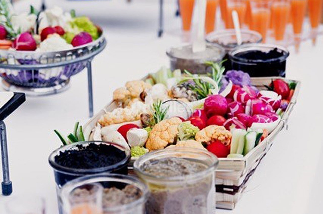 Plateau de légumes colorés avec sauces en pots, présenté sur une table blanche pour un buffet ou apéritif.