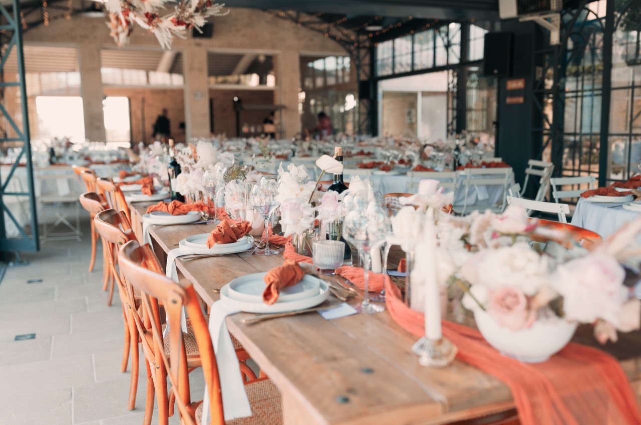 Salle de réception décorée avec des tables en bois, nappes blanches, fleurs et serviettes orange.