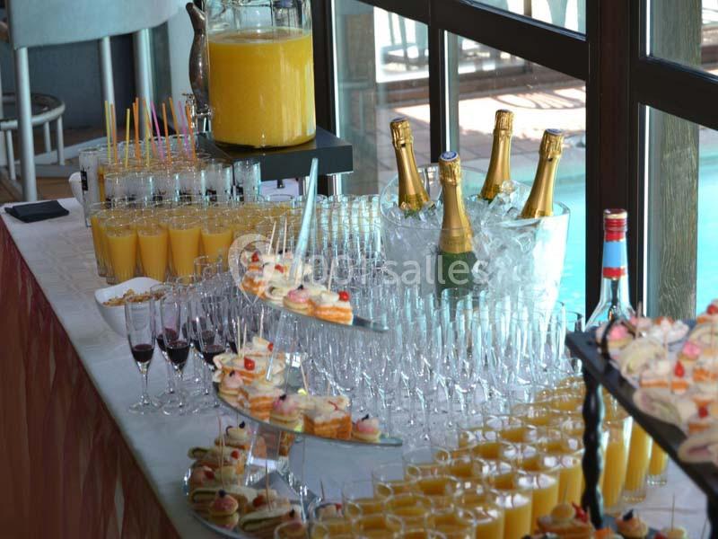Buffet avec jus d'orange, bouteilles de champagne dans la glace, verrines et amuse-bouches sur une table près d'une baie…