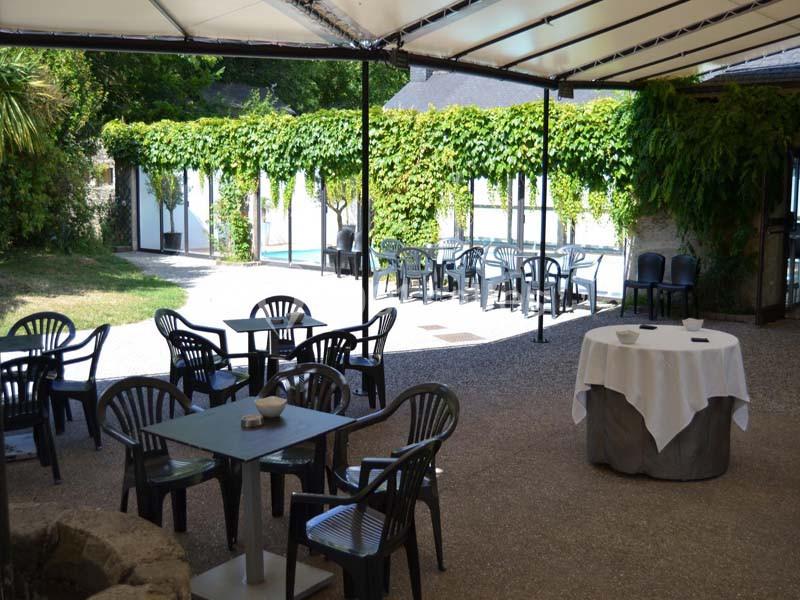 Terrasse extérieure avec tables et chaises en plastique sous une pergola, entourée de murs couverts de végétation.