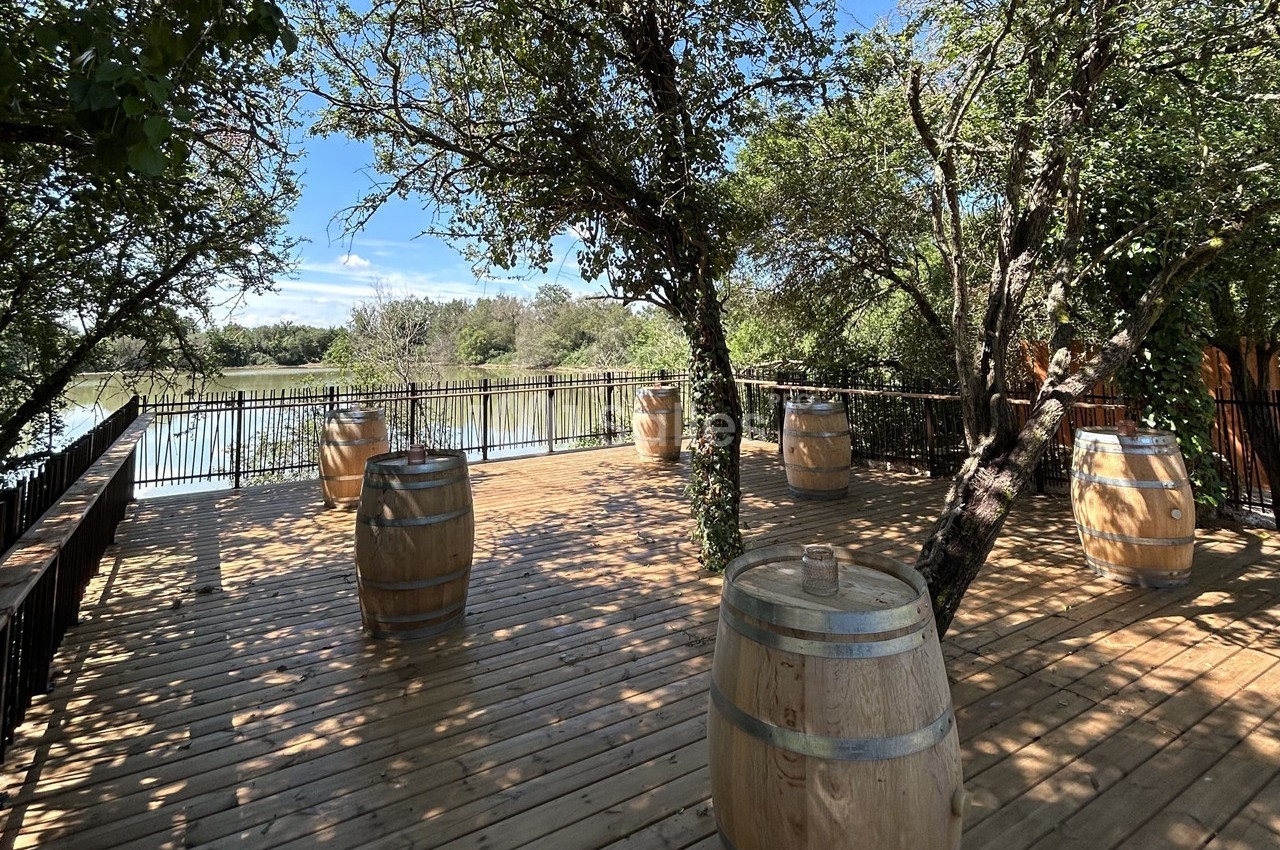 Terrasse en bois avec des tonneaux en décoration, entourée d'arbres et donnant sur un plan d'eau.