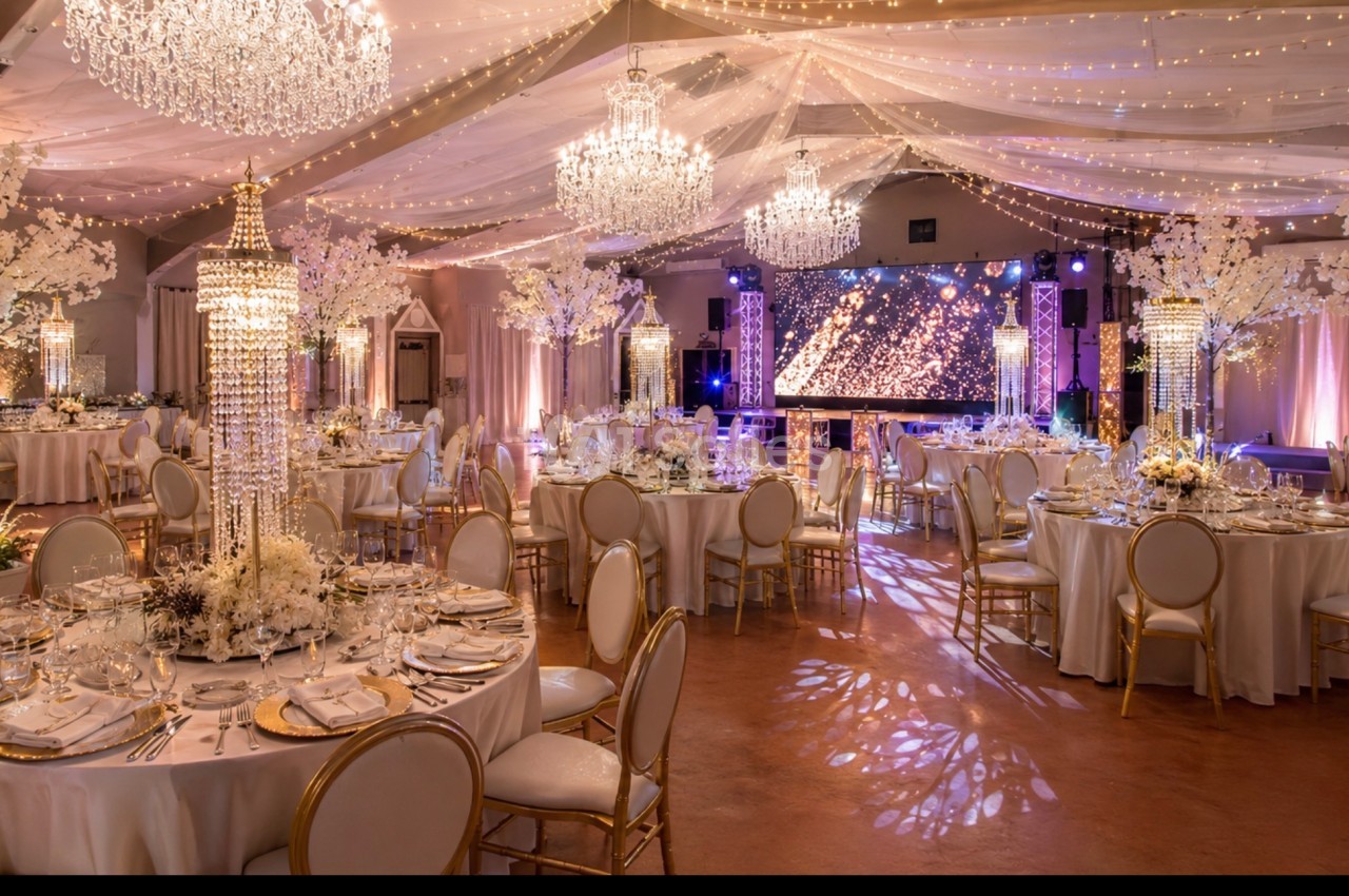 Salle de réception élégante décorée de chandeliers, guirlandes lumineuses et tables dressées pour un événement.