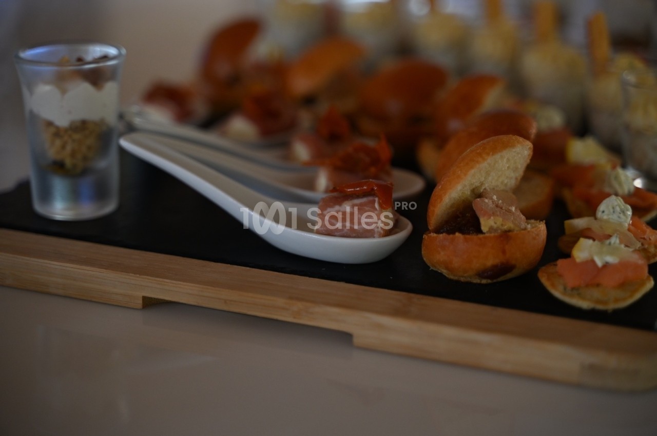 Plateau de dégustation avec verrines, cuillères garnies de charcuterie et mini-sandwichs sur une planche en bois.