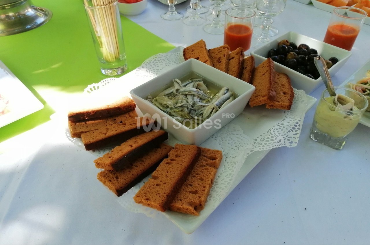 Assiette de toasts avec anchois marinés, olives noires et sauces, présentée sur une table dressée pour un buffet.