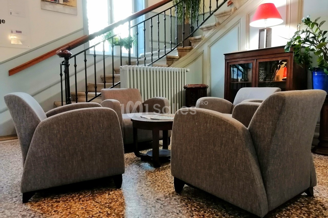 Quatre fauteuils gris disposés autour d'une table basse dans un salon lumineux avec escalier en arrière-plan.