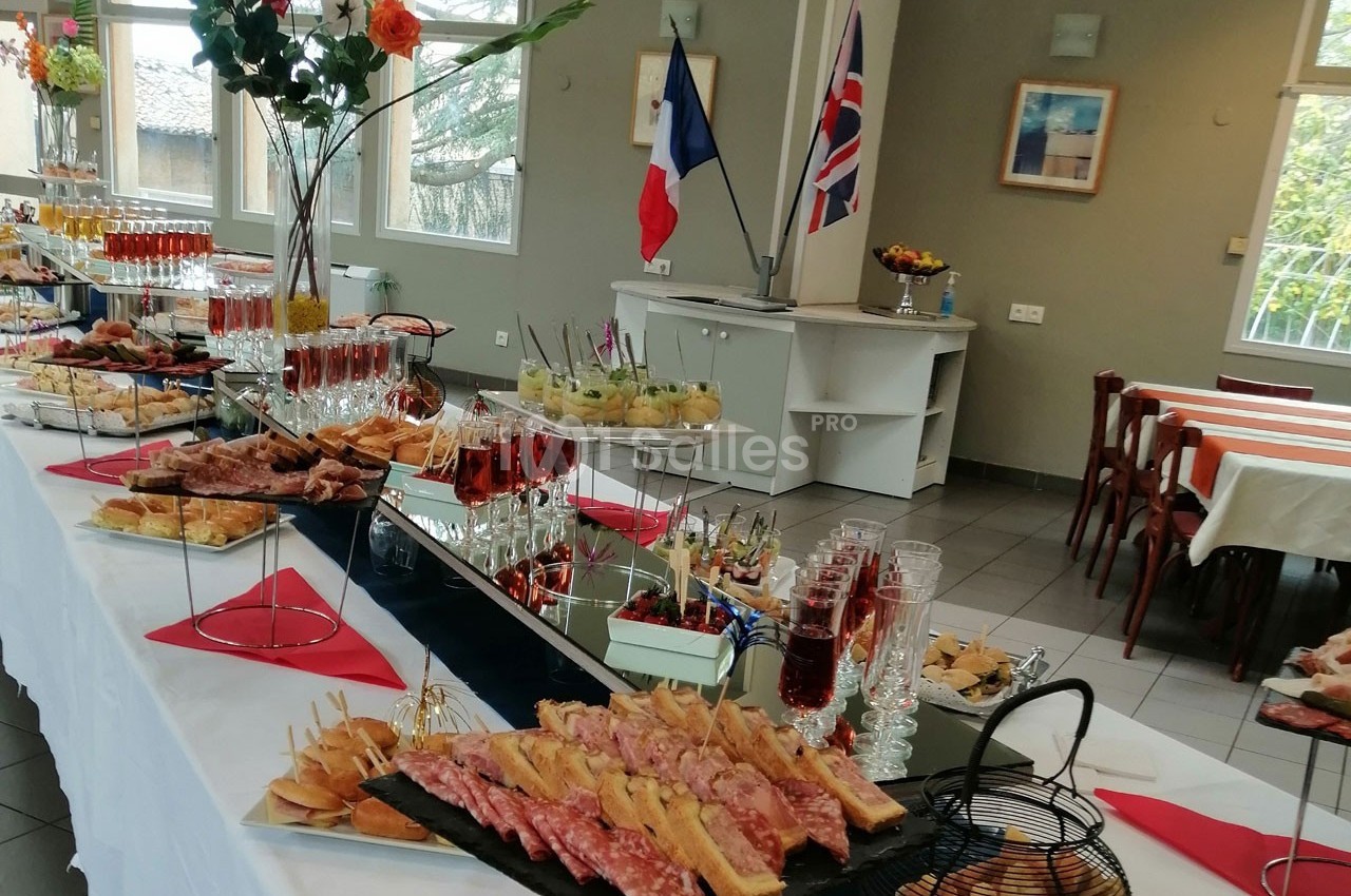 Buffet varié avec charcuterie, verrines et boissons, disposé dans une salle décorée de drapeaux français et britannique.