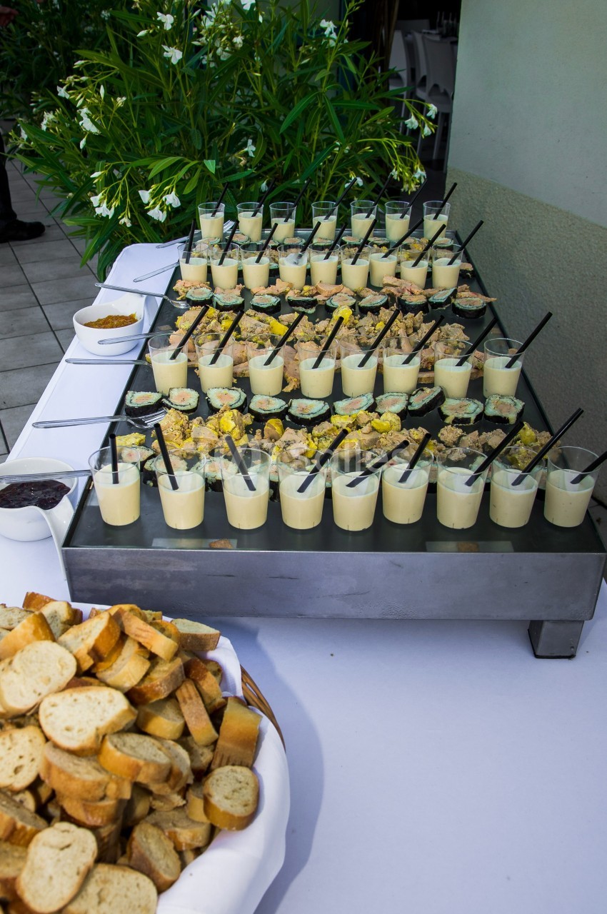 Buffet avec verrines salées garnies de cuillères, accompagnées de pain grillé et de condiments sur une table blanche.