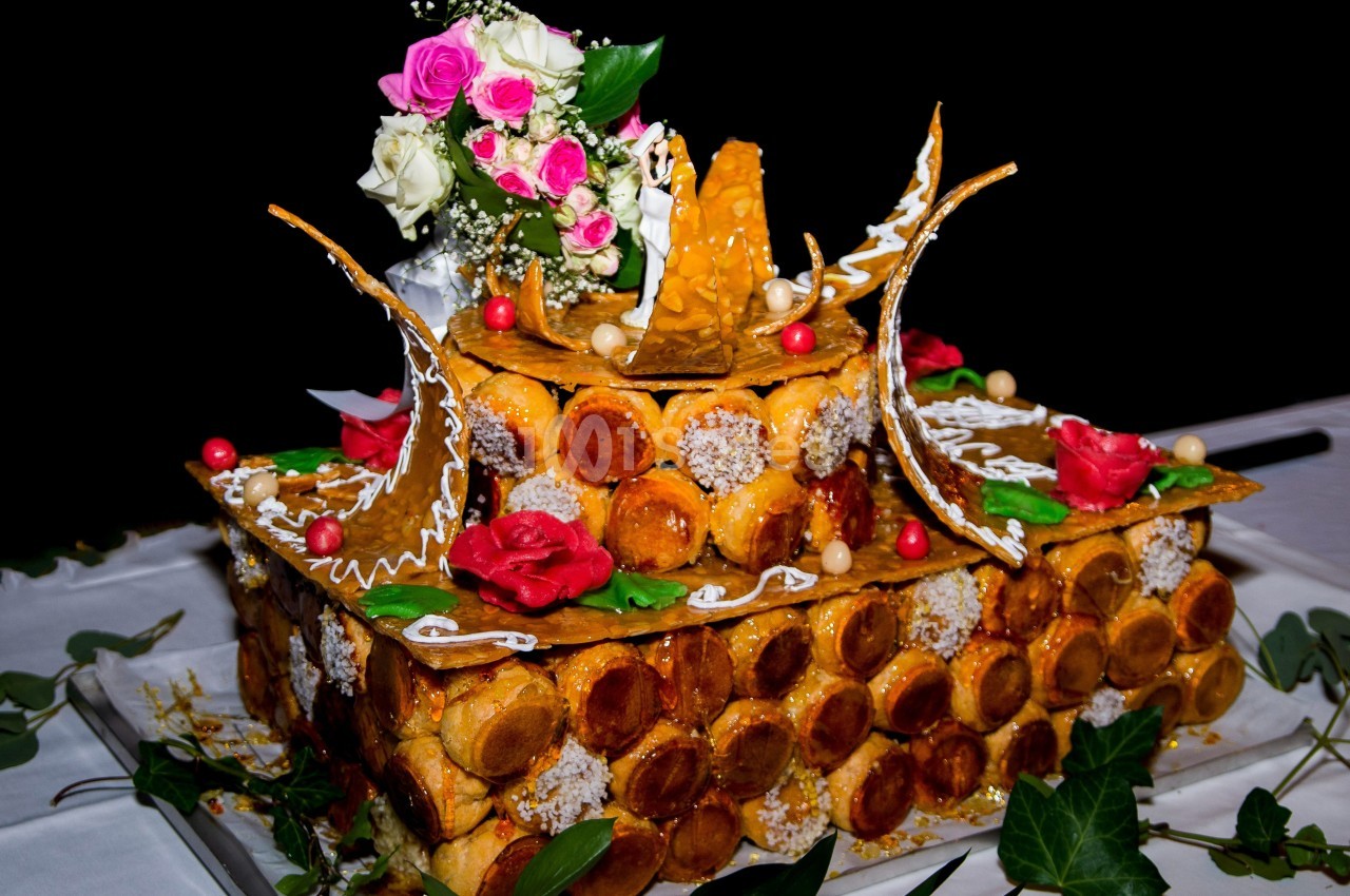 Pièce montée en choux caramélisés décorée de roses, feuilles vertes et éléments en sucre sur une table blanche.