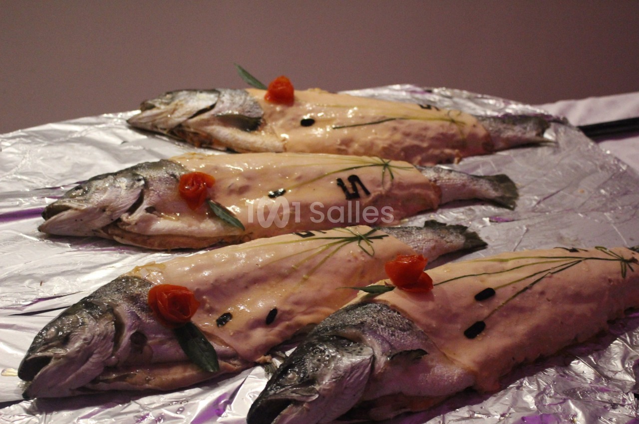 Quatre poissons entiers garnis de pâte et décorés de fines herbes et de fleurs rouges sur une feuille d'aluminium.