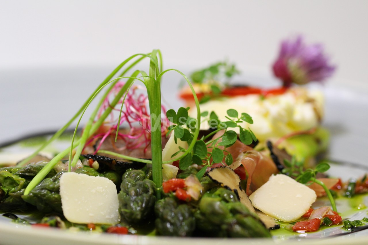 Assiette garnie d'asperges, copeaux de fromage, légumes colorés et herbes fraîches, présentée avec soin.