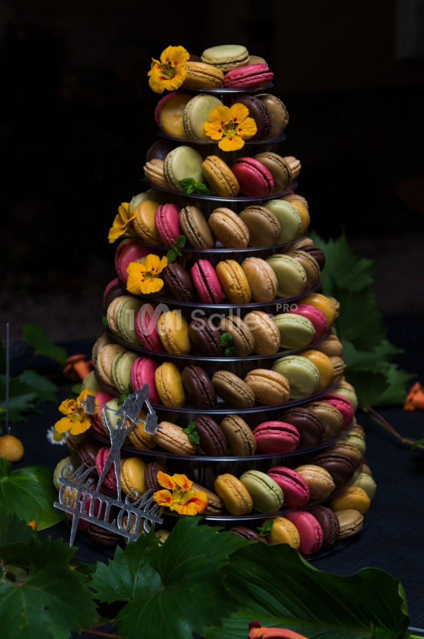 Tour de macarons colorés décorée de fleurs jaunes sur une table sombre avec des feuilles en arrière-plan.