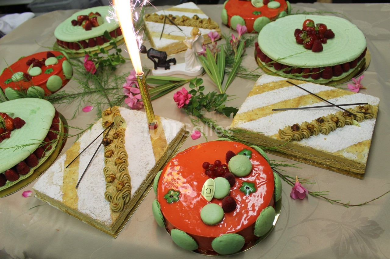 Assortiment de gâteaux décorés avec fruits, macarons et crème, disposés sur une table ornée de fleurs et d'une bougie…