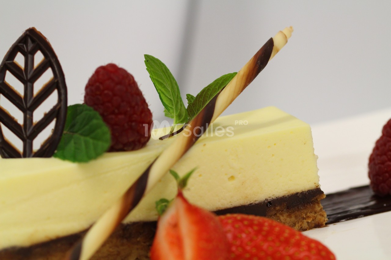Part de gâteau au citron surmontée de framboises, feuilles de menthe, décor en chocolat et fraises en avant-plan.