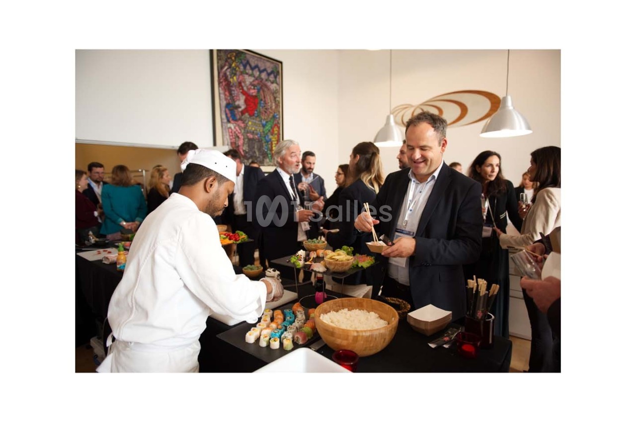 Un chef prépare des sushis pour des invités lors d'un événement professionnel dans une salle lumineuse.