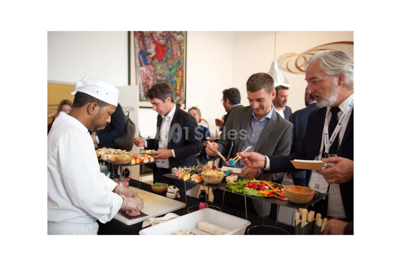 Un chef prépare des plats devant des convives en costume qui se servent à un buffet lors d'un événement.