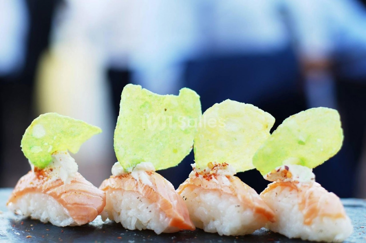 Sushis au saumon garnis de chips vertes, alignés sur une surface sombre avec un arrière-plan flou.
