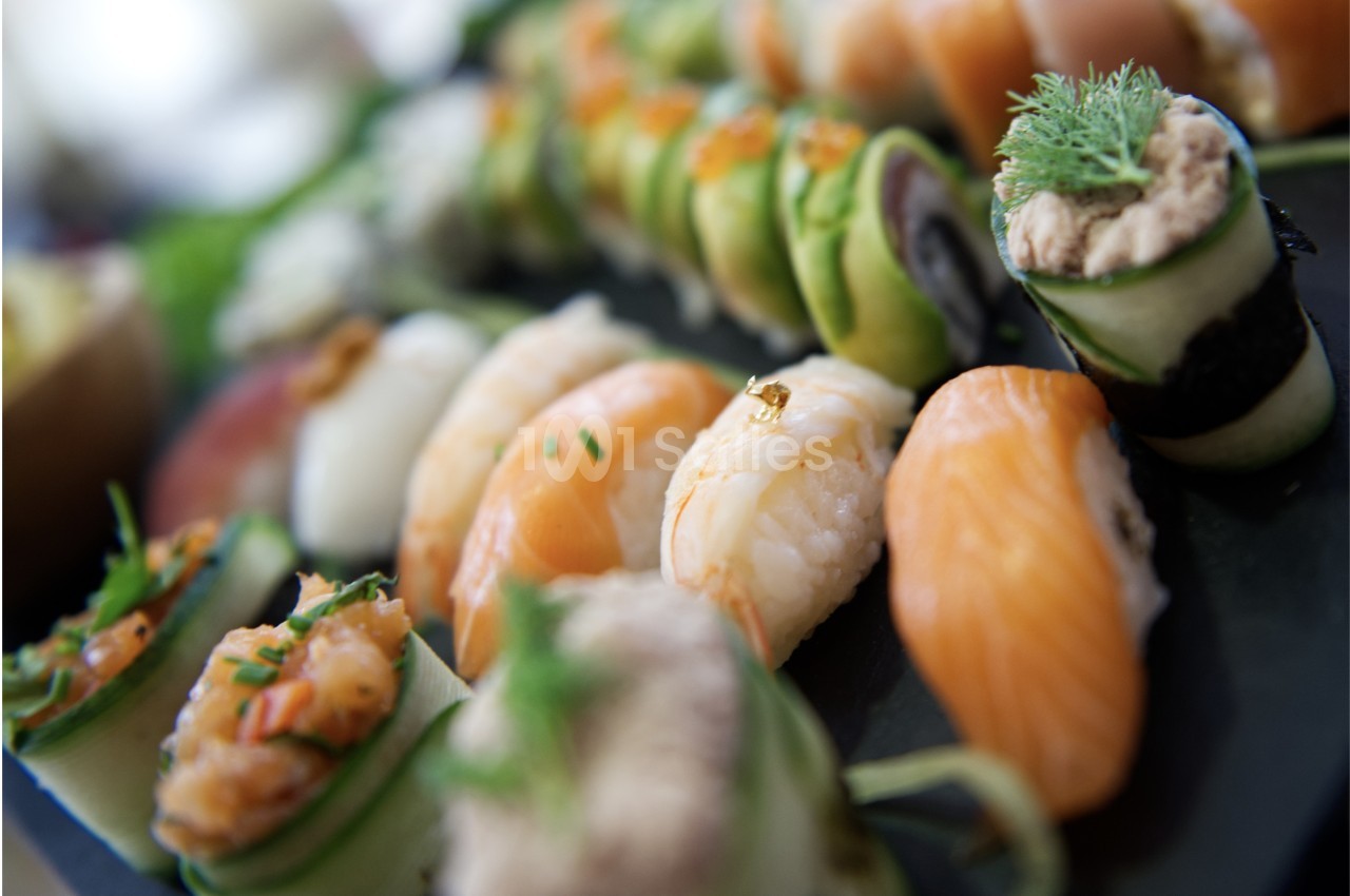 Assortiment de sushis et makis variés présentés sur un plateau noir, décorés avec des herbes et des garnitures.
