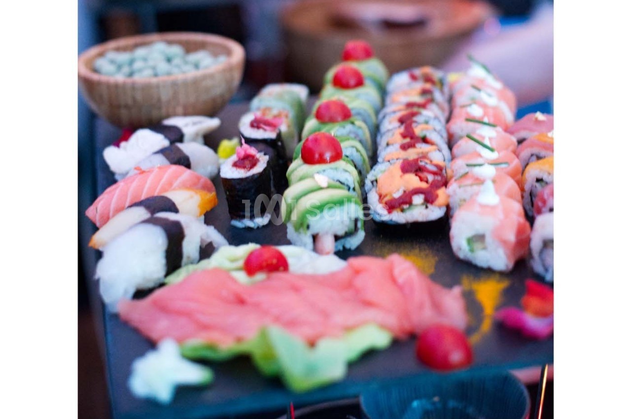 Plateau de sushis variés avec makis, nigiris et sashimis, décorés de tomates cerises et servi sur une ardoise.