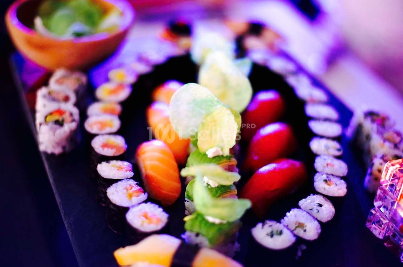 Plateau de sushis variés avec makis, sashimis et chips, présenté sur une table éclairée par une lumière colorée.