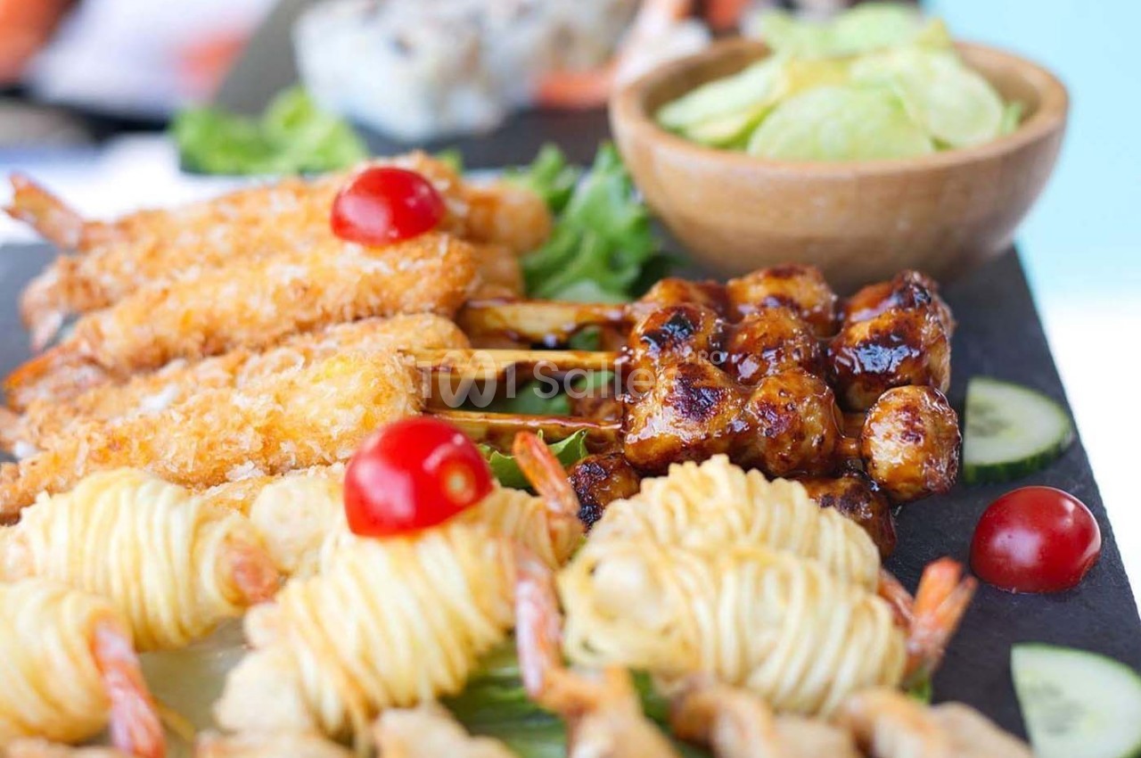 Assortiment de brochettes et bouchées apéritives avec crevettes, légumes et sauce, présenté sur un plateau.