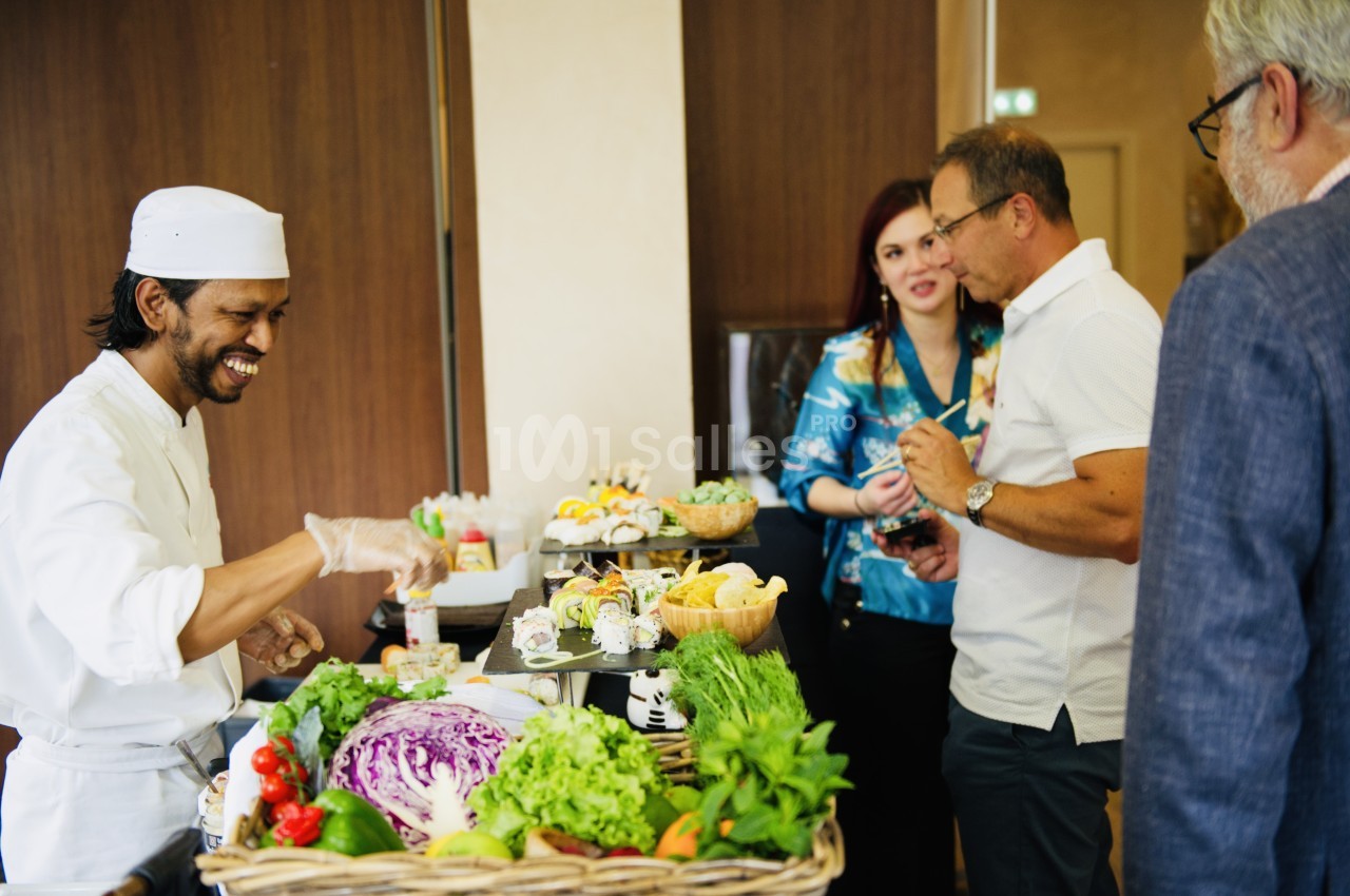 Un chef prépare des plats devant des convives autour d'une table garnie de légumes et d'ingrédients frais.
