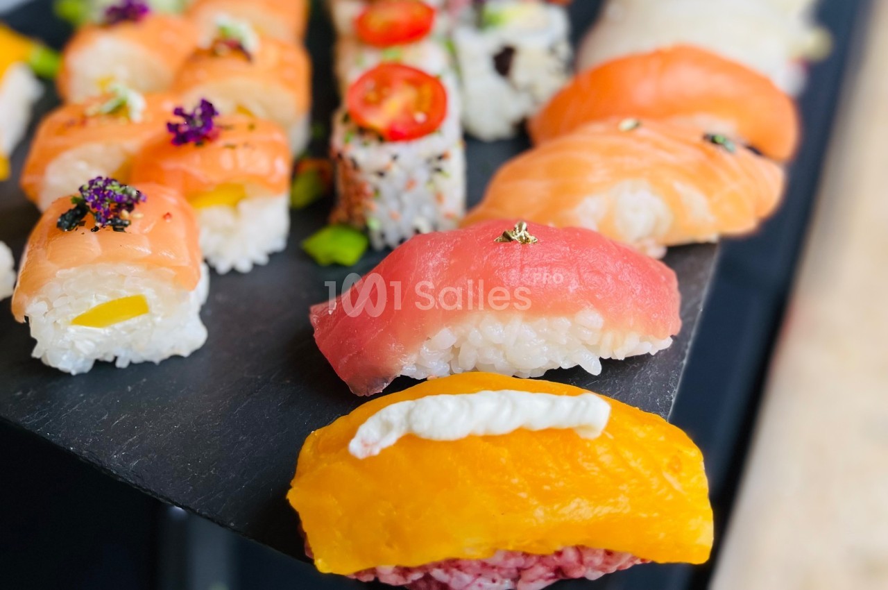 Assortiment de sushis colorés présentés sur une ardoise, avec des garnitures variées comme saumon, mangue et thon.