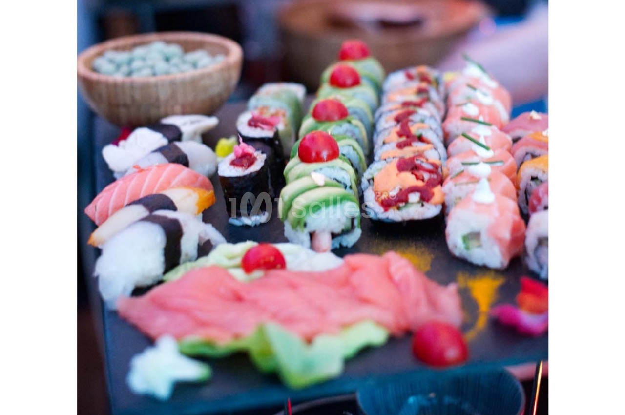 Plateau de sushis variés avec makis, nigiris et sashimis, décorés de tomates cerises et servi sur une ardoise.