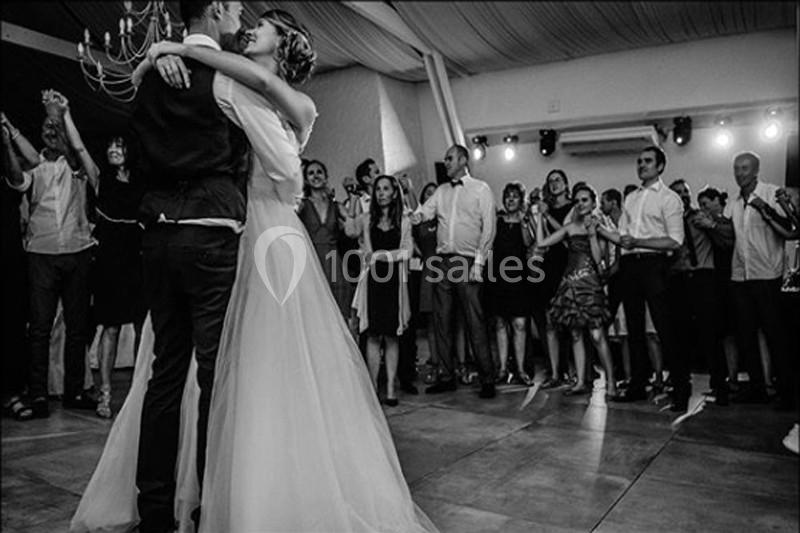 Un couple danse sous les regards des invités dans une salle de réception décorée sobrement.