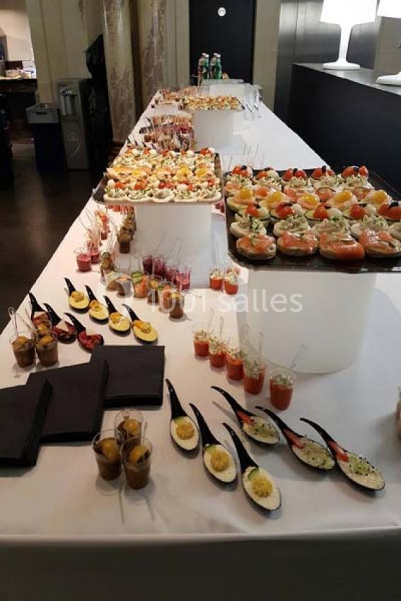 Buffet avec verrines, cuillères apéritives et bouchées variées disposées sur une table blanche.