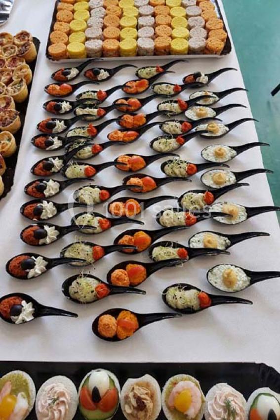 Plateau de cuillères apéritives variées disposées en rangées, accompagné de bouchées et mini-tartelettes.