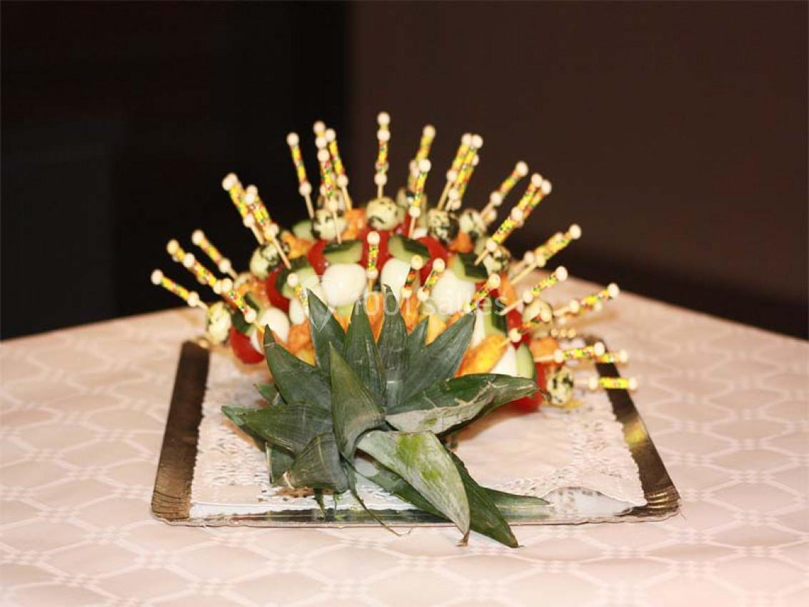 Présentoir de brochettes apéritives colorées sur une base décorative en ananas, posé sur une nappe blanche.