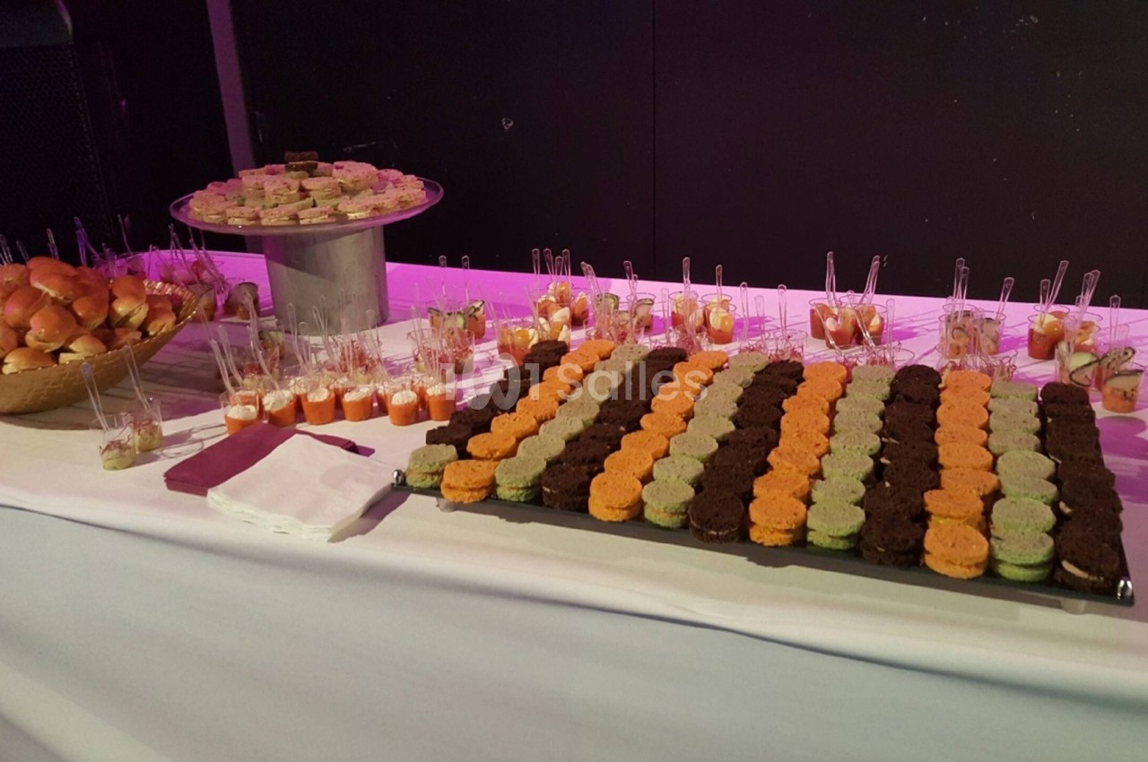 Buffet avec mini-sandwichs, verrines colorées et assortiments de bouchées sucrées et salées sur une table blanche.