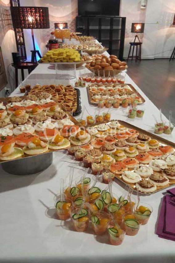 Buffet varié avec assortiments de canapés, verrines, pains et desserts disposés sur une longue table blanche.