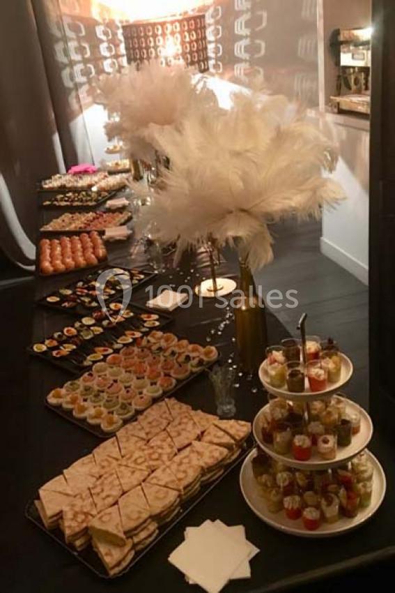 Buffet élégant avec divers amuse-bouches, verrines et décorations de plumes blanches sur une table sombre.