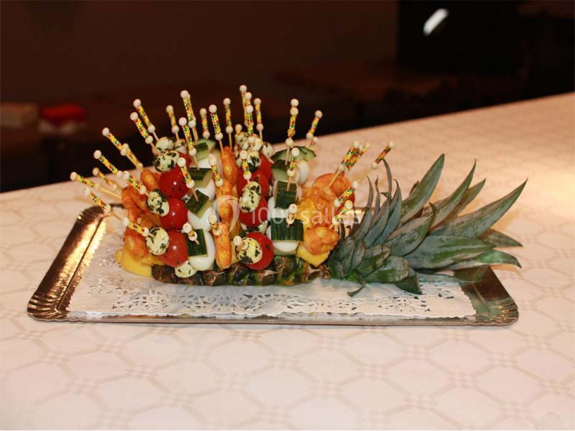 Plateau de brochettes apéritives colorées disposées sur une base d'ananas, présenté sur une nappe blanche.