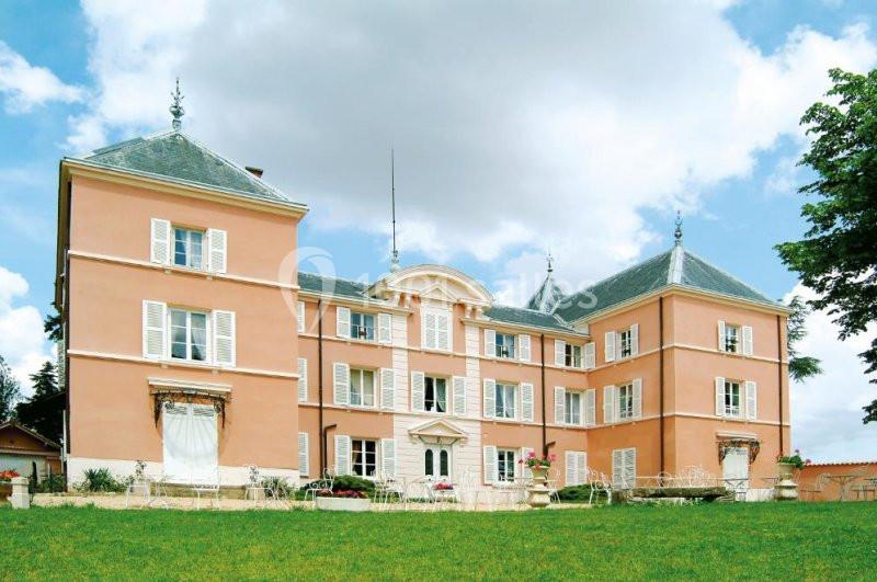Façade d'un grand bâtiment rose à trois étages avec des volets blancs, entouré d'une pelouse et de mobilier de jardin.