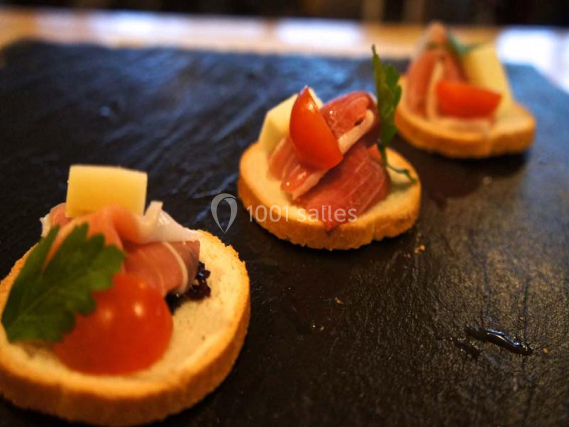 Tranches de pain garnies de jambon cru, fromage, tomate cerise et persil, présentées sur une ardoise noire.