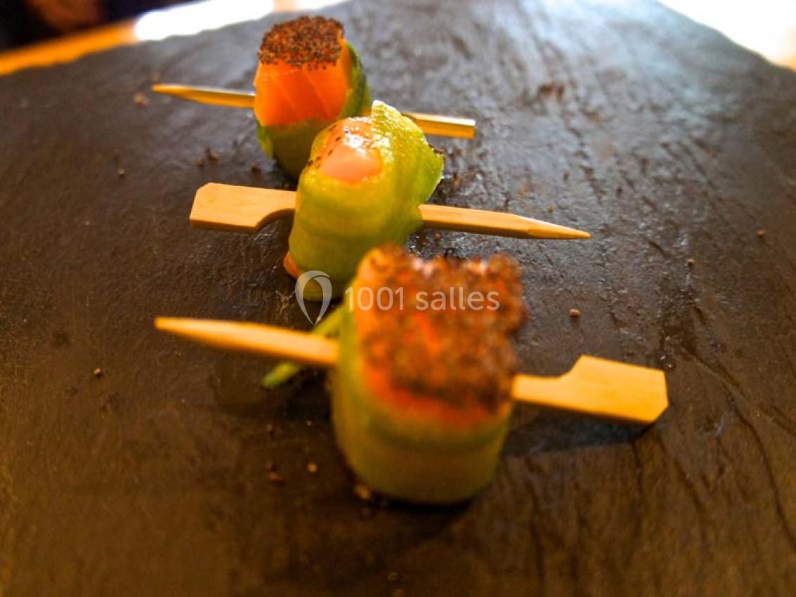 Bouchées de saumon enroulées dans des tranches de concombre, présentées sur des piques en bois sur une ardoise.