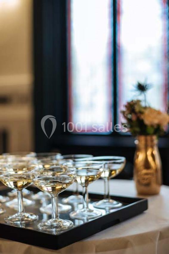 Plateau de coupes de champagne sur une table, avec un vase de fleurs en arrière-plan près d'une fenêtre.
