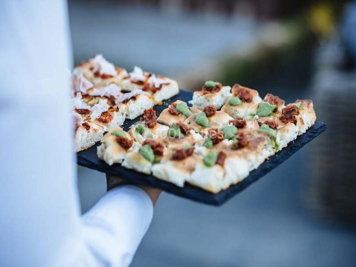Plateau de focaccia garnie de morceaux de viande et d'herbes, tenu par une personne en chemise blanche.