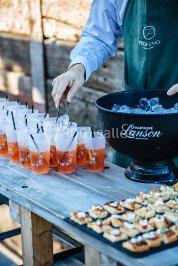 Un serveur remplit des verres de cocktail avec des glaçons près d'un plateau de canapés sur une table en bois.