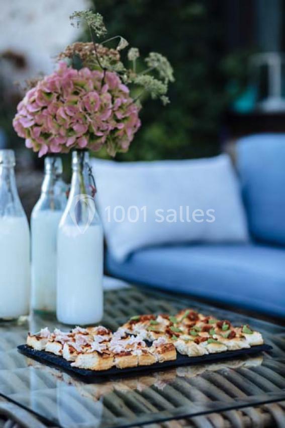 Plateau de toasts variés sur une table en verre, avec des bouteilles de lait et un bouquet d'hortensias en arrière-plan.