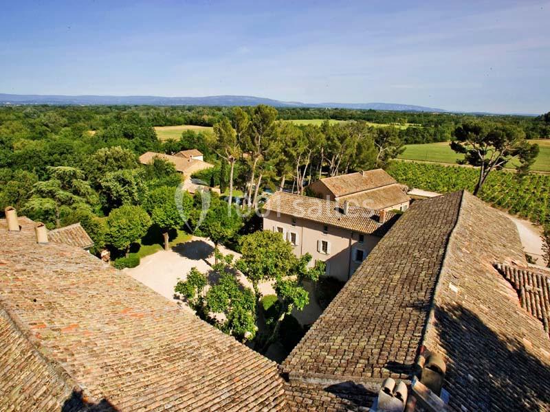 Vue aérienne d'un domaine rural avec des toits en tuiles, des arbres, des vignes et un paysage vallonné en arrière-plan.