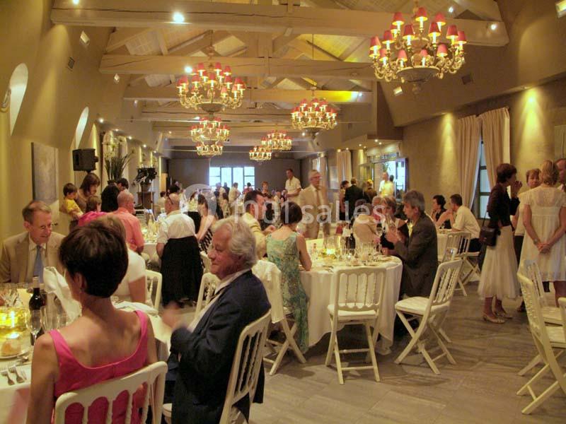 Salle de réception avec des invités assis à des tables rondes, éclairée par des lustres et une lumière chaleureuse.
