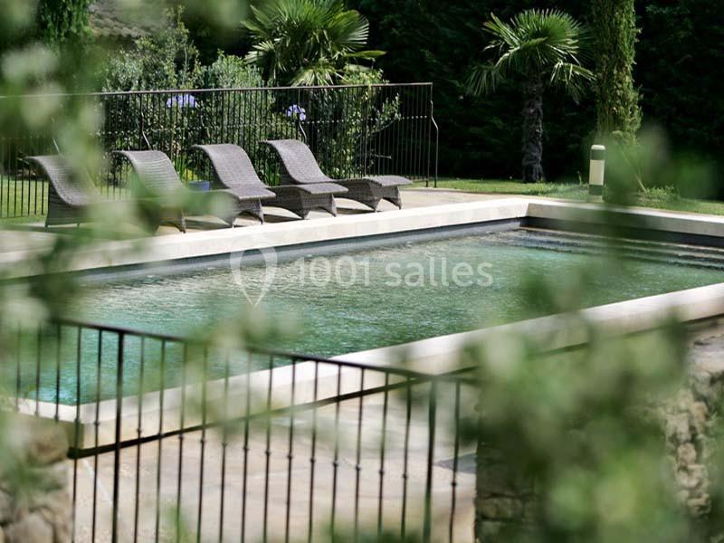 Piscine rectangulaire entourée de chaises longues en rotin, bordée de végétation et d'une clôture métallique.